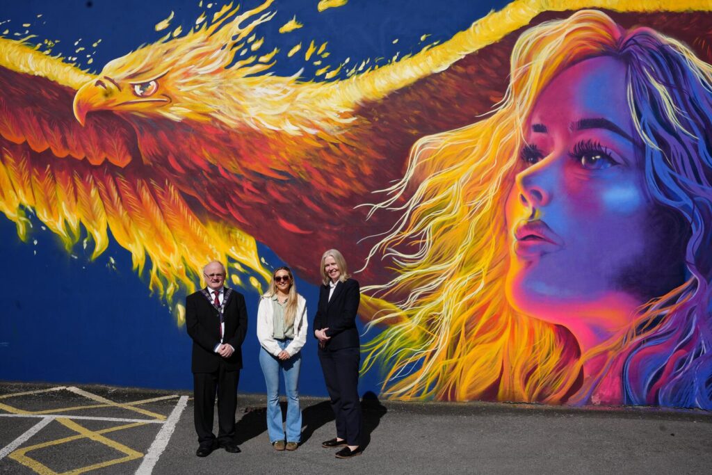 llr Barry McElduff, Chair of Fermanagh and Omagh District Council, Hannah Constance – Mural Artist, and Alison McCullagh Chief Executive of Fermanagh and Omagh District Council stand in front of RISE