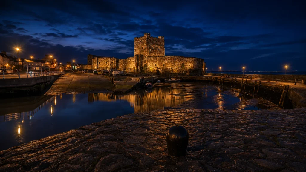 Carrickfergus Castle illuminated beside the waterfront and harbour at night