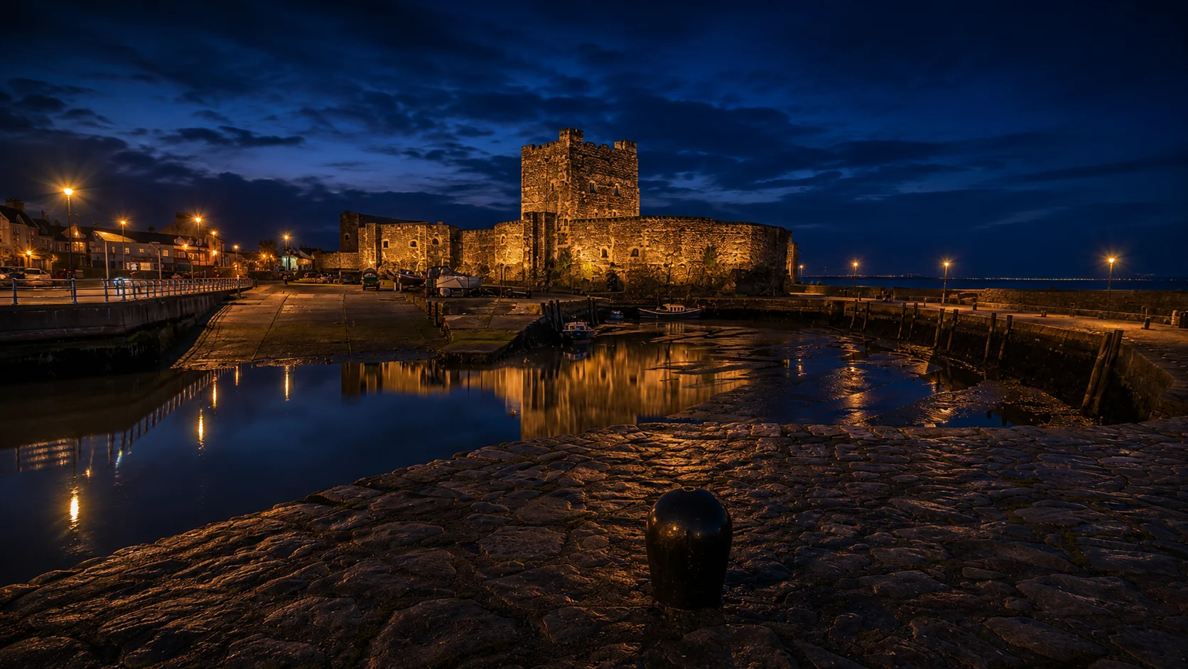 Carrickfergus Castle illuminated beside the waterfront and harbour at night